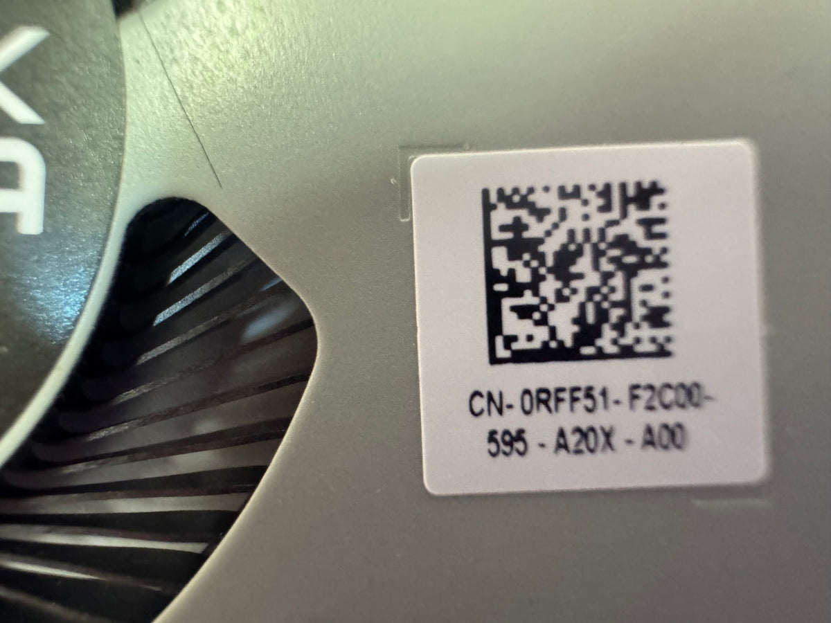 Close-up of a white product label with a QR code and printed alphanumeric text, attached to a metallic silver component next to a dark fan blade.